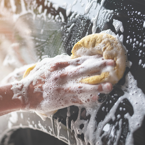 Hand scrubbing a surface with a sponge covered in soap suds.