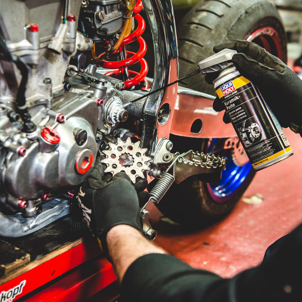 Person working on a motorcycle engine with a can of Liquid Moly Karamik Paste