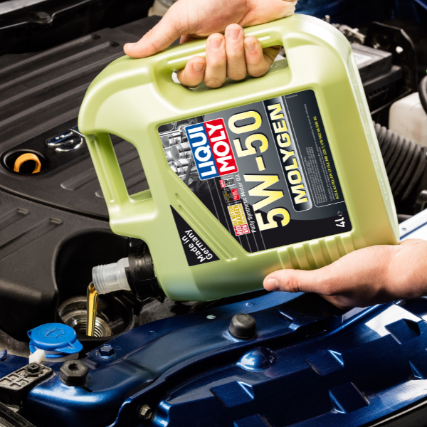 Person holding a green bottle of Liqui Moly 5W-50 Molygen oil near an open car hood.