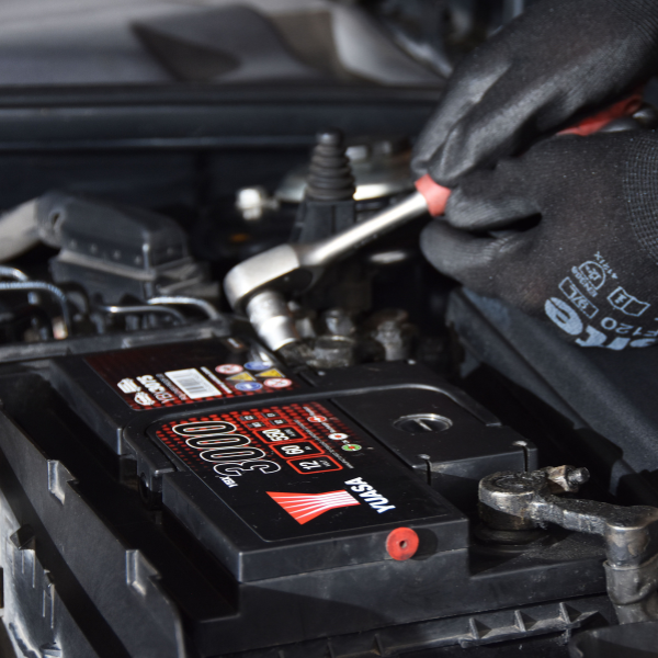 Person working on a Yuasa battery with tools, wearing gloves.
